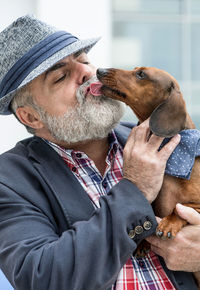 Close-up of mature man holding dog while standing outdoors