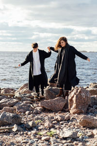 Friends standing on rock by sea against sky