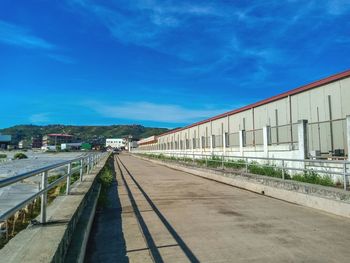 Empty road by buildings against blue sky