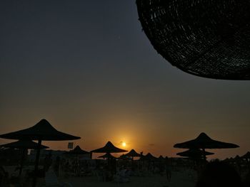 Silhouette parasols on beach against sky during sunset