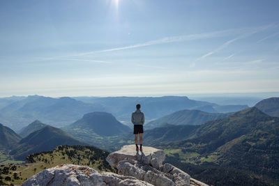 Rear view of man standing on cliff against sky