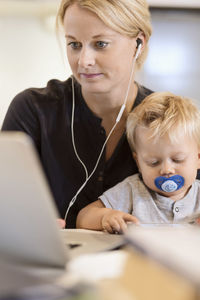 Mother with baby boy listening music on laptop at home