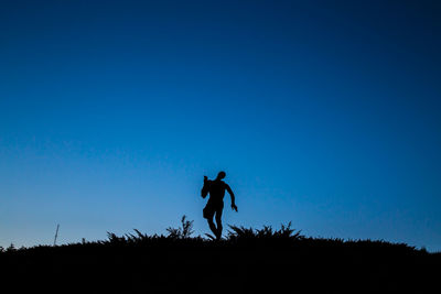 Silhouette man standing on field against clear blue sky