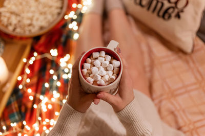 Cup of cocoa or coffee drink with marshmallows in female holding hands over the legs of woman
