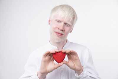 Portrait of young woman holding heart shape over white background