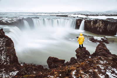 Rear view of man standing on rock while looking at waterfall