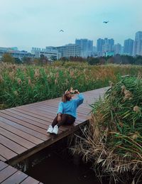 Woman sitting on grass in city against sky