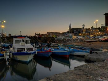 Boats moored in harbor at sunset