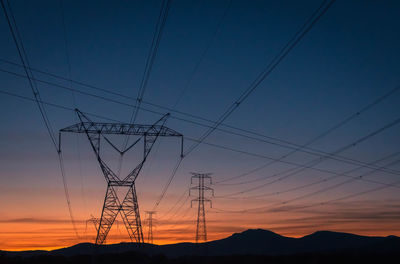 Low angle view of silhouette electricity pylons against sky at sunset
