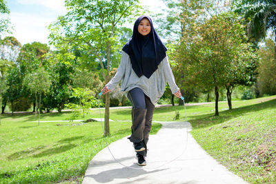 Full length portrait of smiling young woman against trees