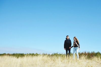 Young couple walking on grassy field against clear sky