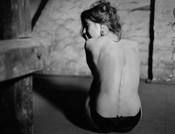 Rear view of sad naked woman sitting in darkroom