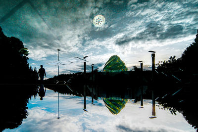 Reflection of silhouette trees in swimming pool against sky