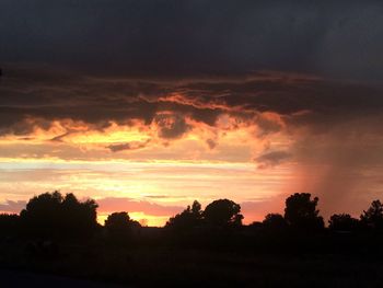 Silhouette trees against dramatic sky during sunset