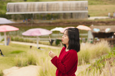 Side view of young woman blowing plant while standing on field