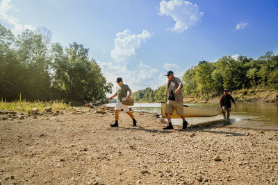 Male friends with boat walking towards lakeshore