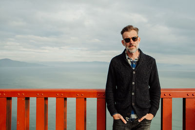 Mature adult male with beard man standing by railing against sea against sky