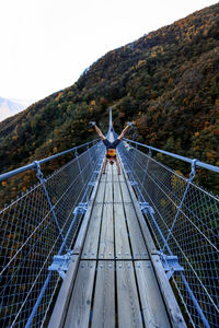 Man doing handstand on footbridge over mountain against sky