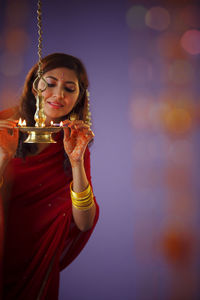 Beautiful indian woman in red sari lighting diya during diwali