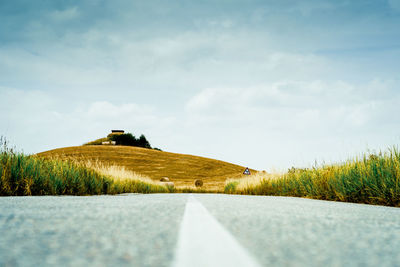 Surface level of road amidst field against sky