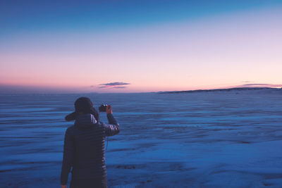 Rear view of men photographing frozen lake against sky during sunset