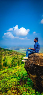 Man sitting on mountain against sky