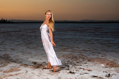 Woman standing at beach against sky during sunset