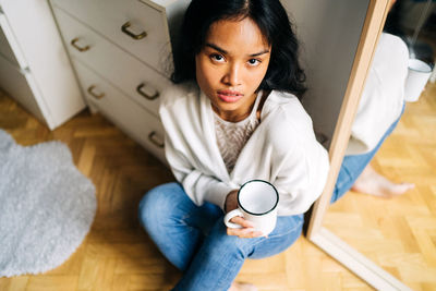 Portrait of young woman holding coffee cup on floor at home
