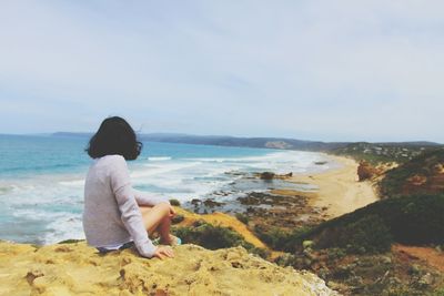 Rear view of man sitting on rocks at beach