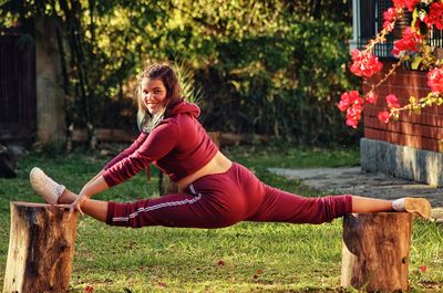 Rear view portrait of teenage girl doing split on tree stumps in yard