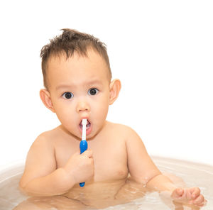 Portrait of shirtless baby boy brushing teeth while sitting in tub