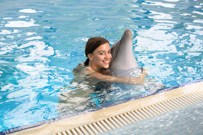 Portrait of smiling young woman with dolphin swimming in pool