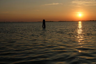 Silhouette person on sea against sky during sunset