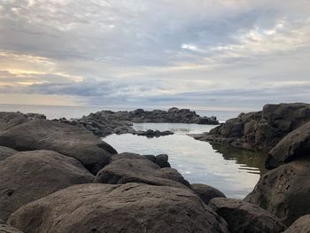 Rocks by sea against sky during sunset