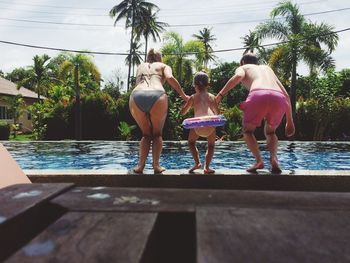 Rear view of parents holding daughter hands while diving in swimming pool during sunny day