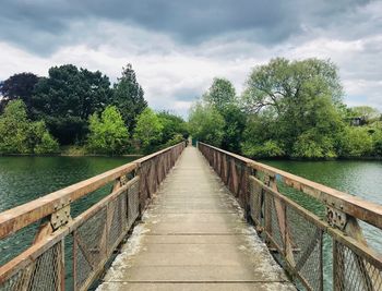 Footbridge along trees and plants against sky