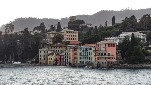 Houses by river and buildings in town against sky