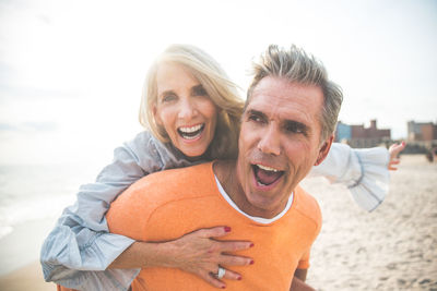 Close-up of man giving piggyback ride to happy girlfriend standing at beach