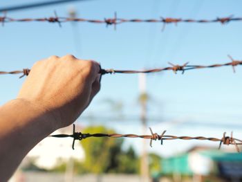 Close-up of hand holding barbed wire against sky