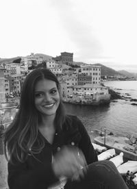 Portrait of smiling young woman in city against sky