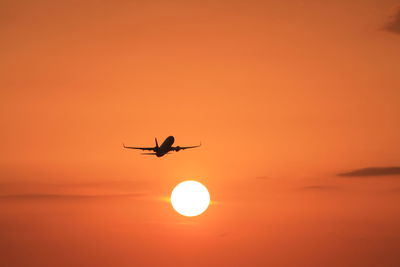 Low angle view of silhouette airplane flying against orange sky