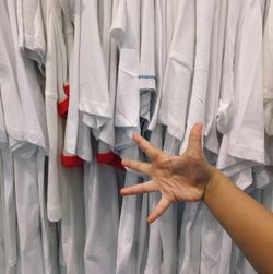 Cropped hand of woman gesturing against t-shirts in store