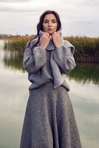 Woman stands next to the lake in a sweater and a scarf in the fall