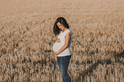 Smiling pregnant woman with hands on stomach standing on field