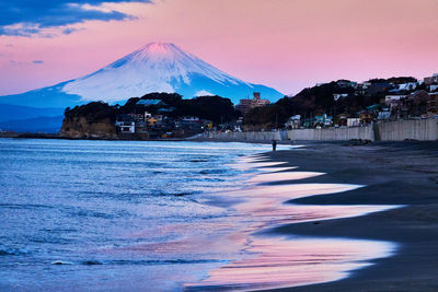 Scenic view of sea and snowcapped mountain against pink moody sky during sunrise