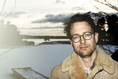 Close-up portrait of mid adult man standing on snow covered field against sky during sunset