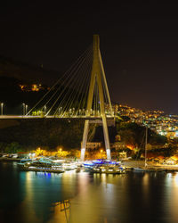 Illuminated bridge over river against sky at night