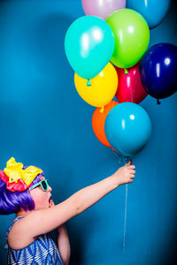 Low section of woman holding colorful balloons against blue wall