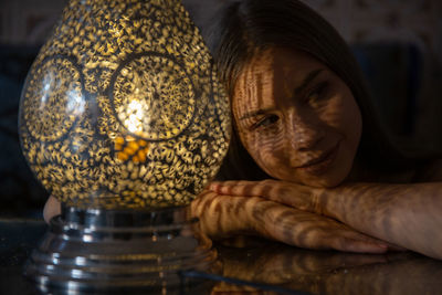 Portrait of young woman sitting against illuminated lamp at home