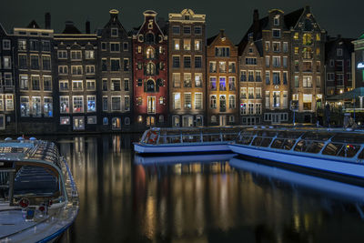 Traditonal houses and cruise boats at the damrak in amsterdam in the netherlands by night